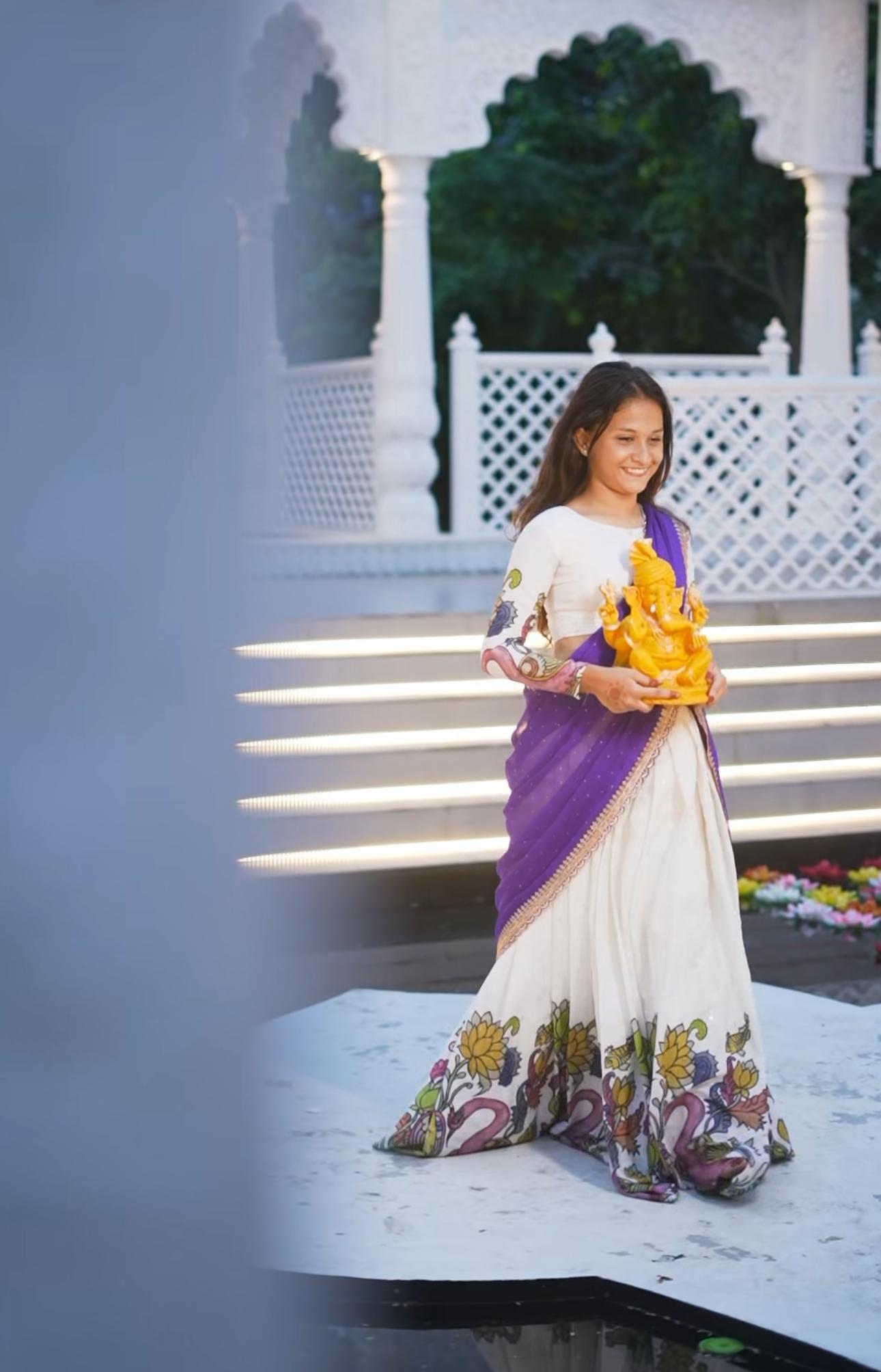 White and purple half saree with floral embroidered hem and gold deity statue