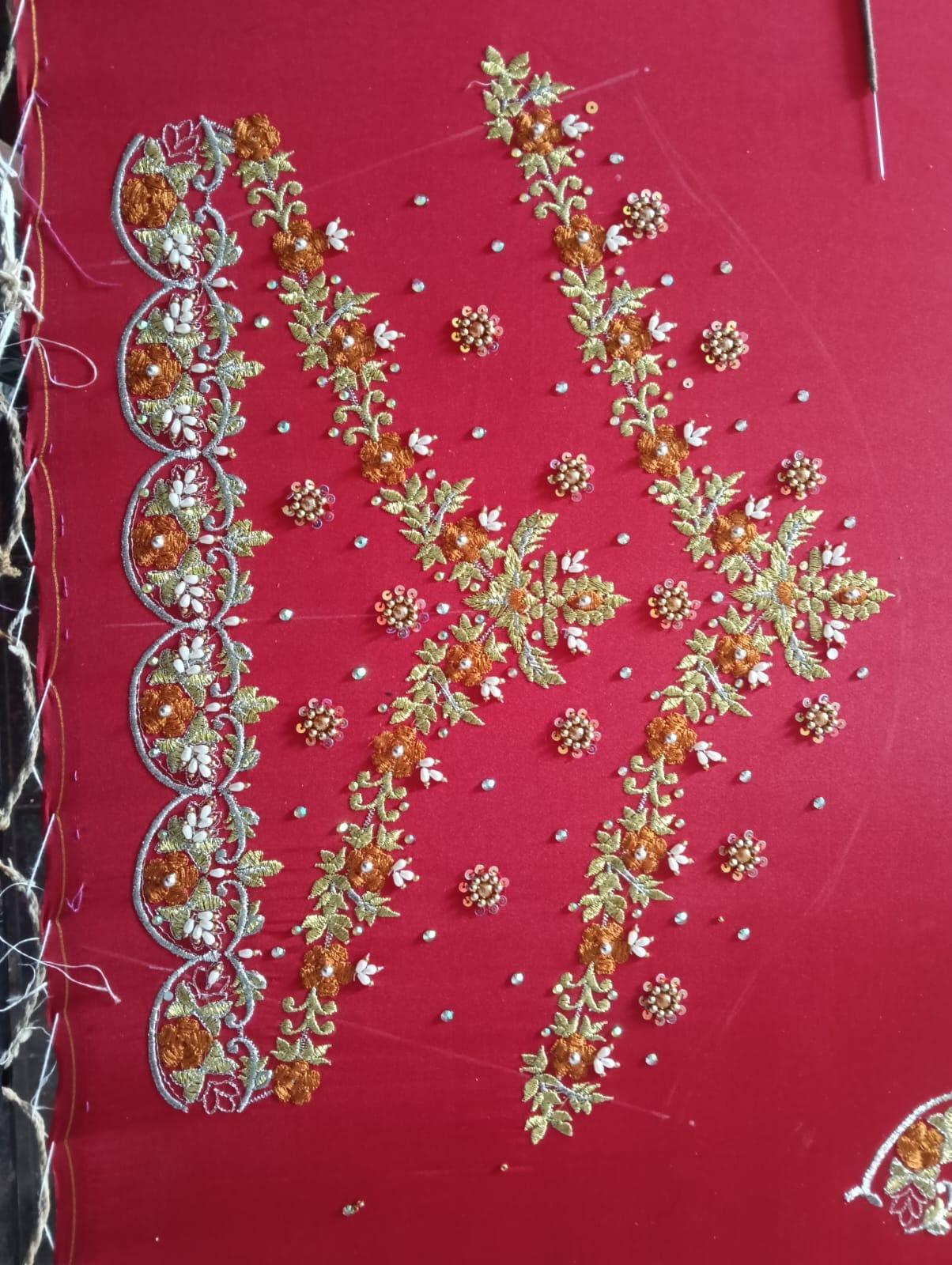Red fabric with golden floral embroidery, zari work, and pearl beadwork