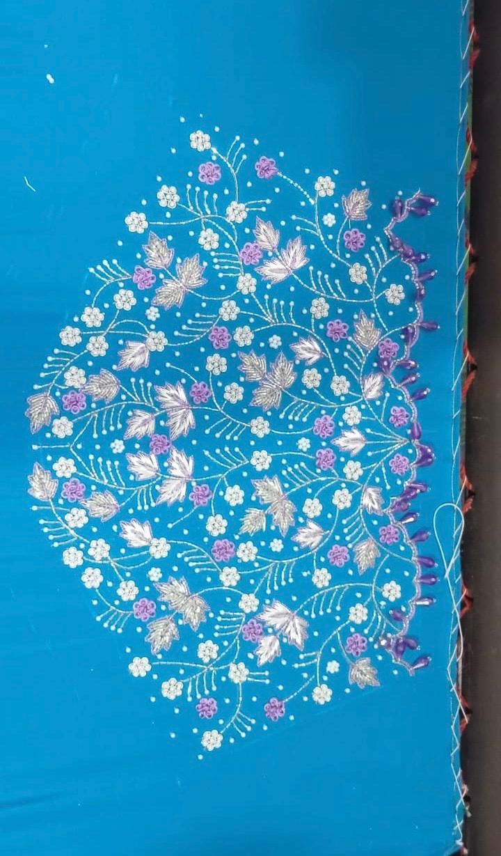 Blue fabric with intricate floral embroidery in white, pink, and purple threads