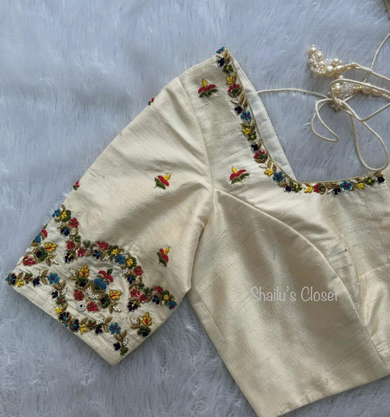 Cream blouse featuring delicate colorful floral embroidery, perfect for elegant and light festive saree styling.