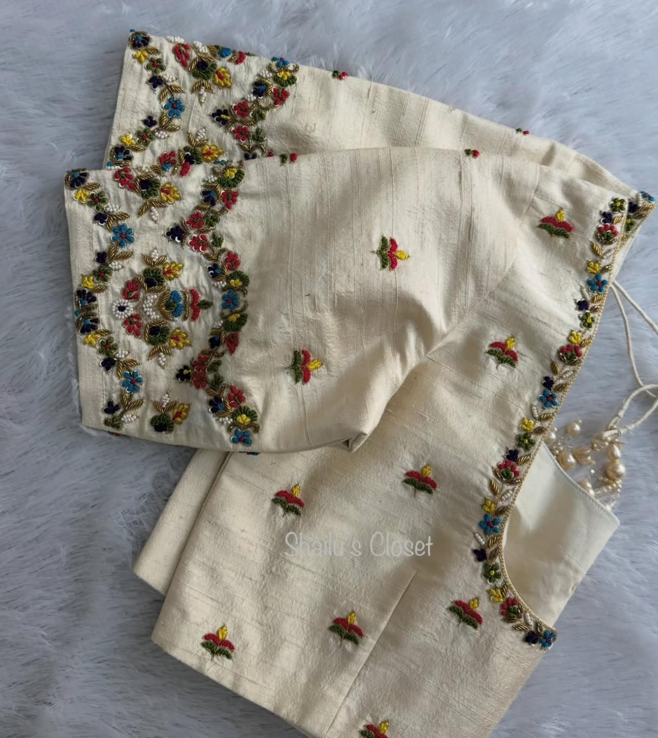 Cream designer blouse with heavy floral embroidery along the neckline and sleeves, suitable for wedding and partywear sarees.